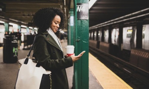 woman with a cup of coffee texts on subway station platform